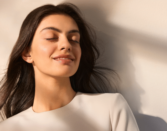 Djevojka se sunča zatvorenih očiju, naslonjena na zid, preksrivena zrakama sunca i sjenama