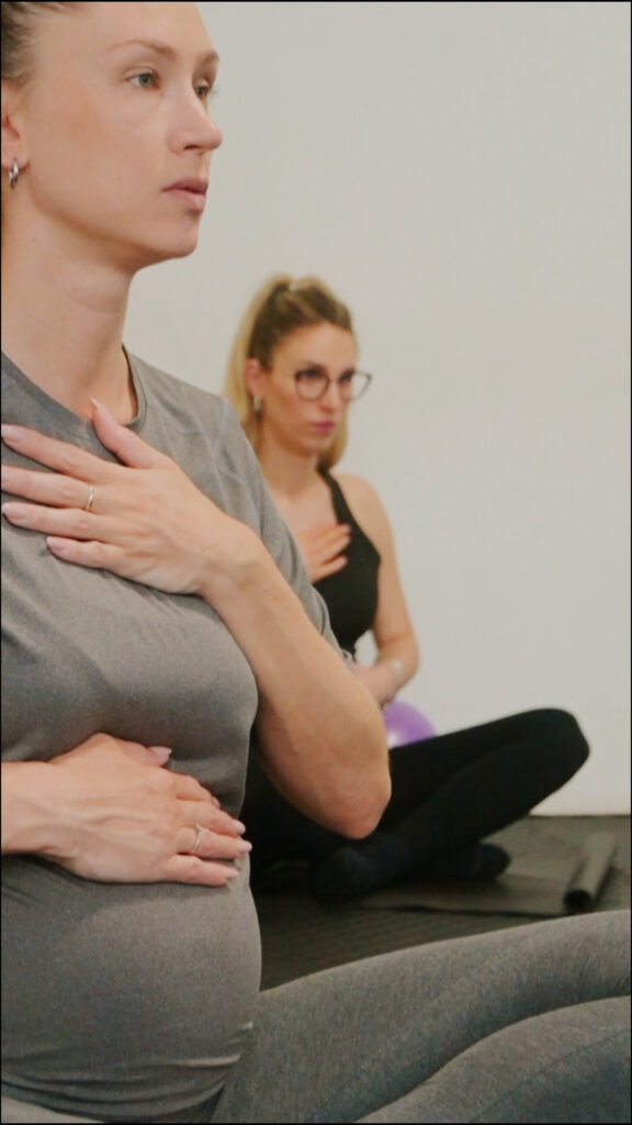 Dvije mame izvode vježbe disanja na podlozi za vježbanje tijekom programa za mame i bebe