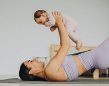 majka u predivnom ljubičastom setu drži bebicu u rukama na podlozi za vježbanje, BEBAiOna