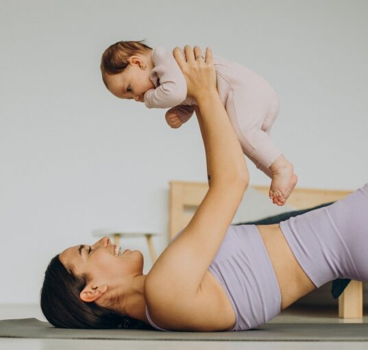 majka u predivnom ljubičastom setu drži bebicu u rukama na podlozi za vježbanje, BEBAiOna