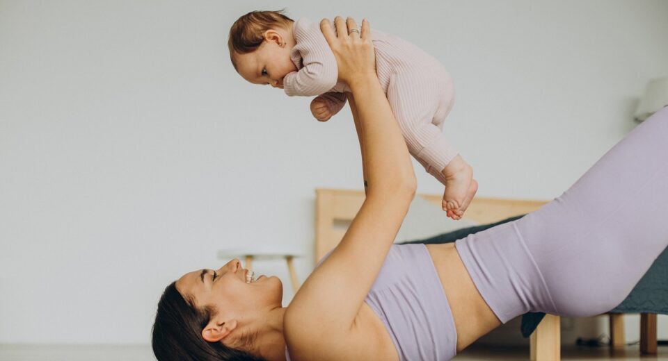majka u predivnom ljubičastom setu drži bebicu u rukama na podlozi za vježbanje, BEBAiOna