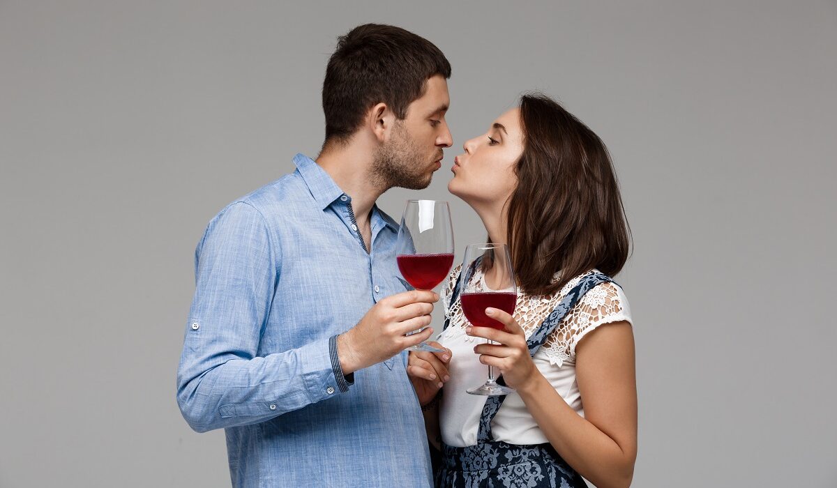 Partneri piju vino i šalju si poljubac il pusu ispred sivog zida